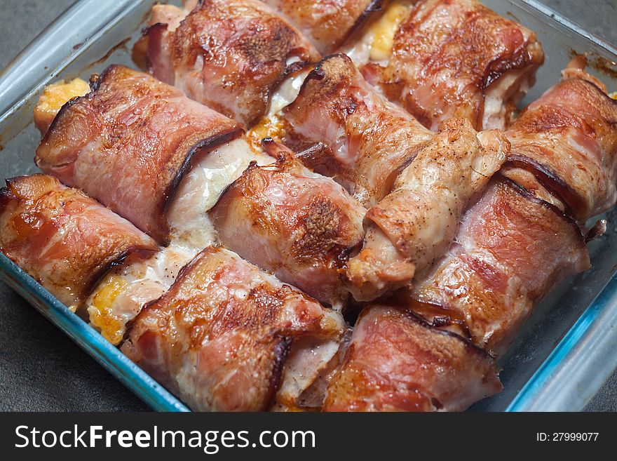 A pile of baked rolls of chicken meat wrapped in pieces of bacon. A pile of baked rolls of chicken meat wrapped in pieces of bacon