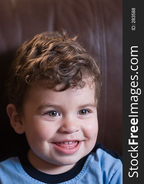 Head and shoulders portrait of young boy toddler smiling sitting on a brown coach. Head and shoulders portrait of young boy toddler smiling sitting on a brown coach.