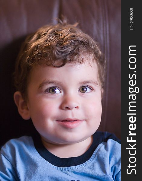 Head and shoulders portrait of young boy toddler with a curious sitting on a brown coach. Head and shoulders portrait of young boy toddler with a curious sitting on a brown coach.