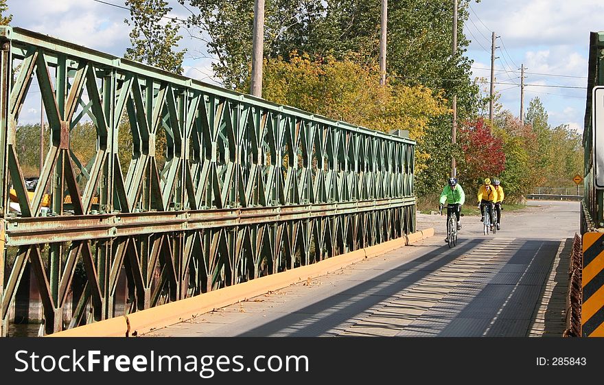 Three cyclists crossing a bridge. There are hydro lines in the background. Three cyclists crossing a bridge. There are hydro lines in the background