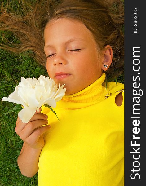 Little girl with a white flower lying on a green grass