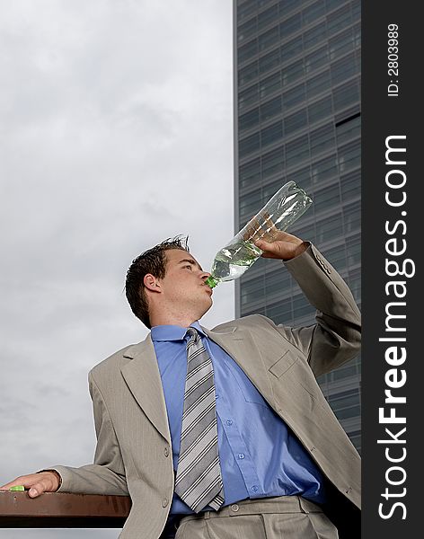Businessman drinking water from plastic bottle in front of business building.