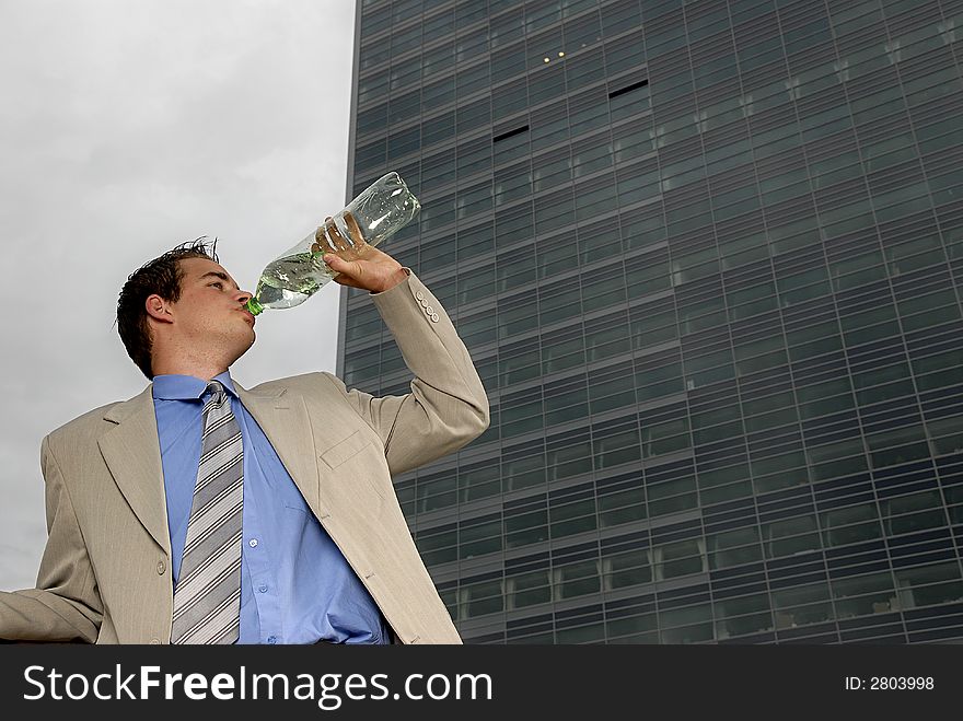 Businessman drinking water from plastic bottle in front of business building.