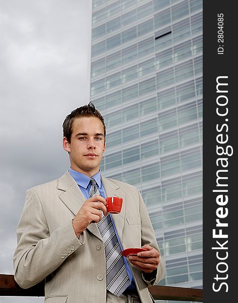 Young businessman having a break and drinking cup of coffee in front of business building. Young businessman having a break and drinking cup of coffee in front of business building.