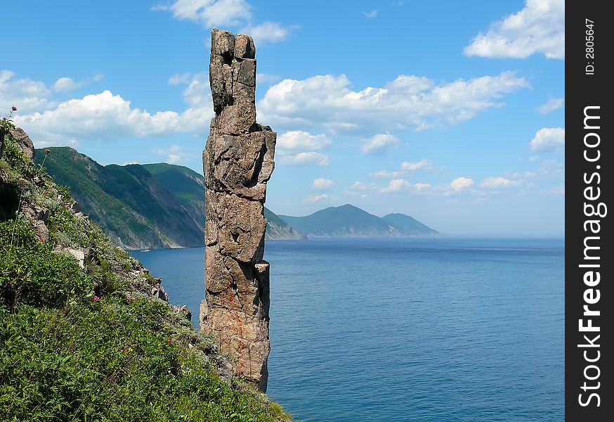 On foreground the single vertical rock with name Hare. On background turquoise sea, cliffs and sky with white clouds. Russian Far Easr, Primorye, Japanese sea, Tasovaya Bay. On foreground the single vertical rock with name Hare. On background turquoise sea, cliffs and sky with white clouds. Russian Far Easr, Primorye, Japanese sea, Tasovaya Bay.