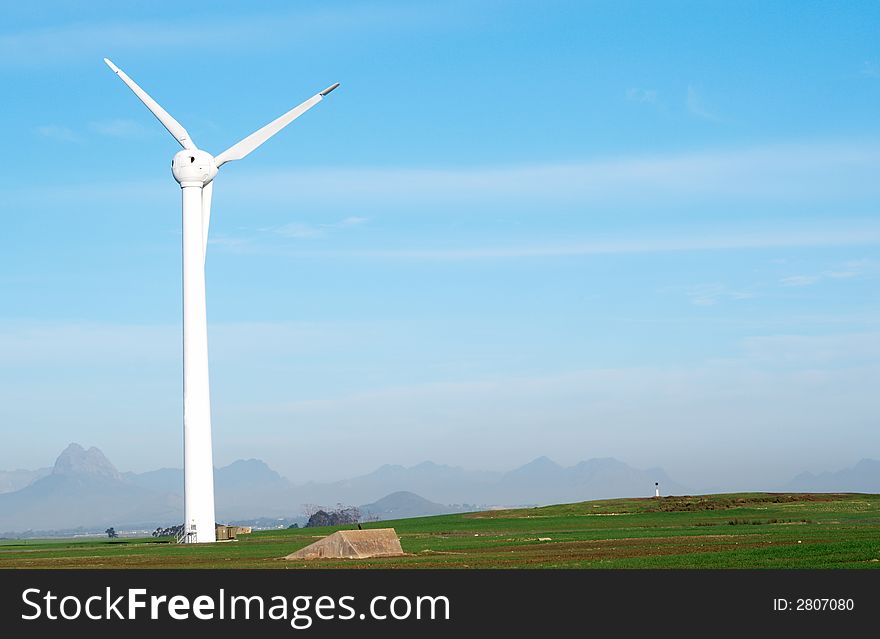 Wind powered electricity generator standing against the blue sky in a green field on the wind farm. Wind powered electricity generator standing against the blue sky in a green field on the wind farm