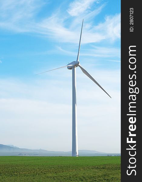 Wind powered electricity generator standing against the blue sky in a green field on the wind farm. Wind powered electricity generator standing against the blue sky in a green field on the wind farm