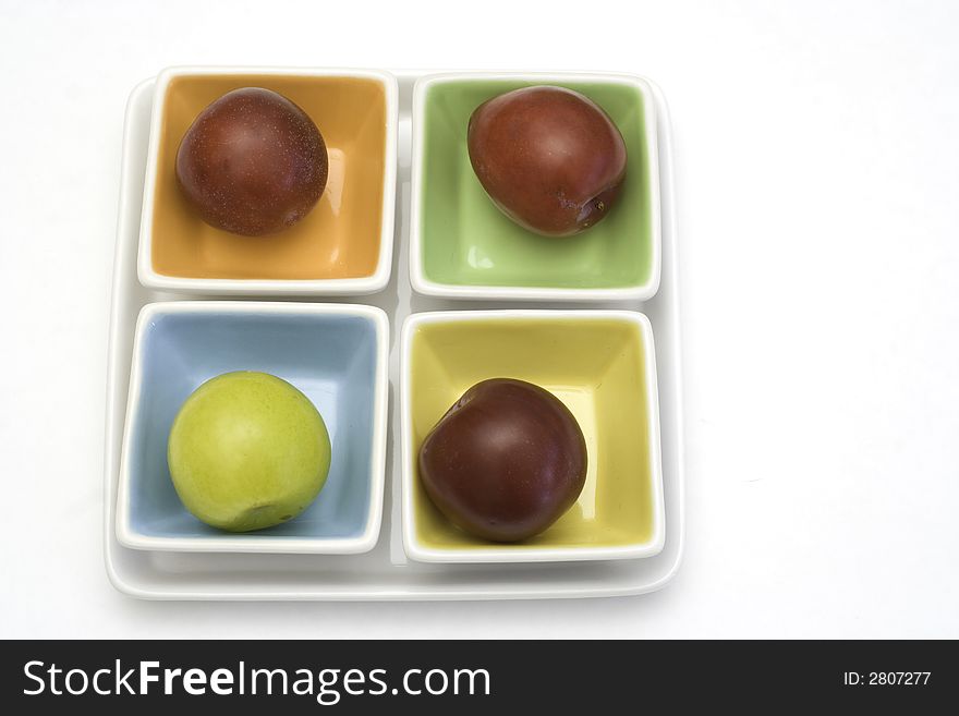 One yellow and three red plums on colorful plates. One yellow and three red plums on colorful plates.