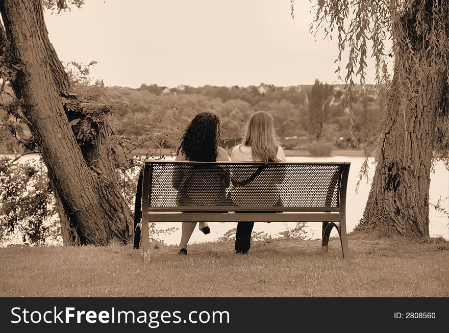Two girls sitting on a bench in a park. Two girls sitting on a bench in a park