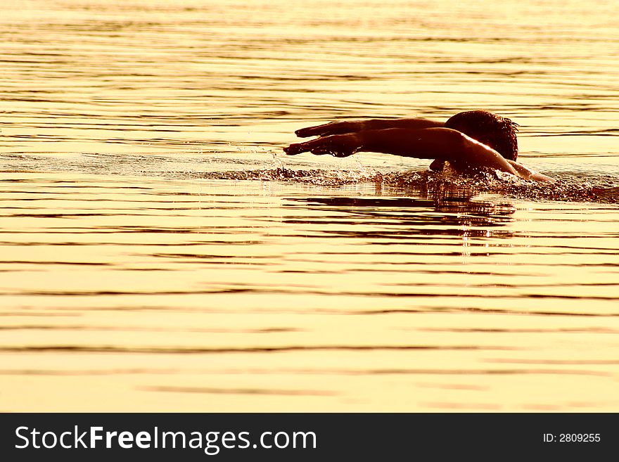 High contrast image of a man diving into lake water during golden sunset, detailed splashes under hands. High contrast image of a man diving into lake water during golden sunset, detailed splashes under hands