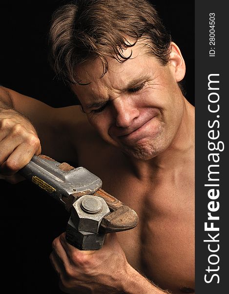 Muscular shirtless man struggles to loosen a big nut with a pipe wrench. Muscular shirtless man struggles to loosen a big nut with a pipe wrench