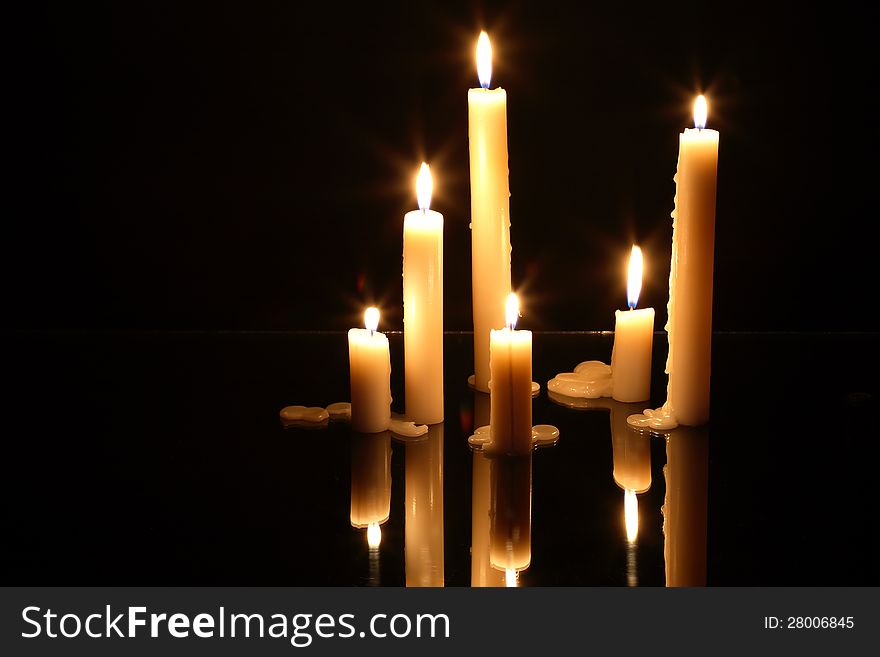 Few lighting candles on glass surface with reflection