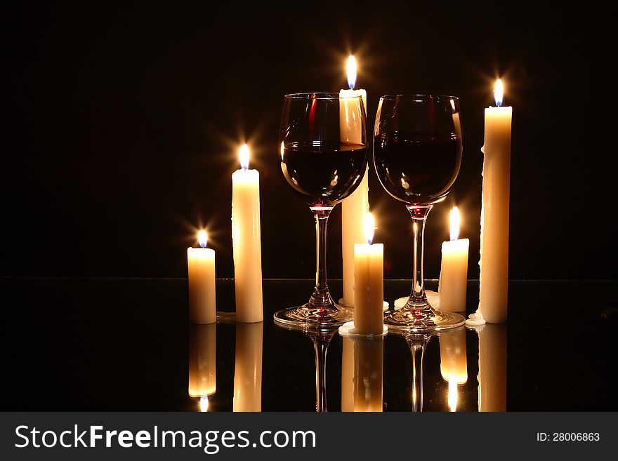 Two elegant goblets of red wine near lighting candles on dark background. Two elegant goblets of red wine near lighting candles on dark background