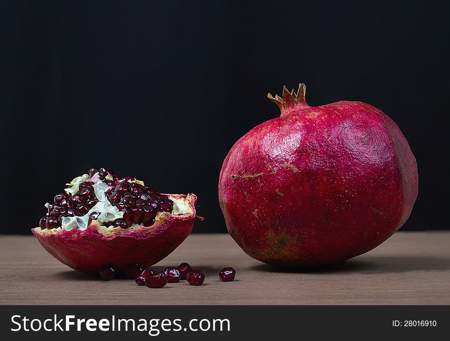 Whole and slice of ripe pomegranate on a black background.
