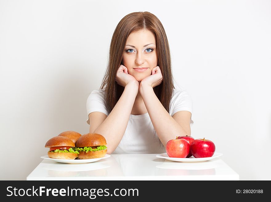 Woman sitting behind the table with standing junk food and apples. Woman sitting behind the table with standing junk food and apples