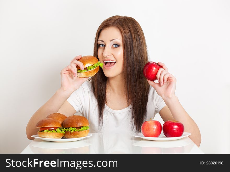 Woman try to eat a hamburger and holding apple to. Woman try to eat a hamburger and holding apple to