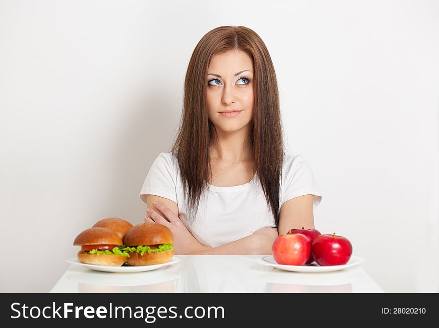 Woman sitting behind the table with standing junk food and apples and thinking what to choose. Woman sitting behind the table with standing junk food and apples and thinking what to choose