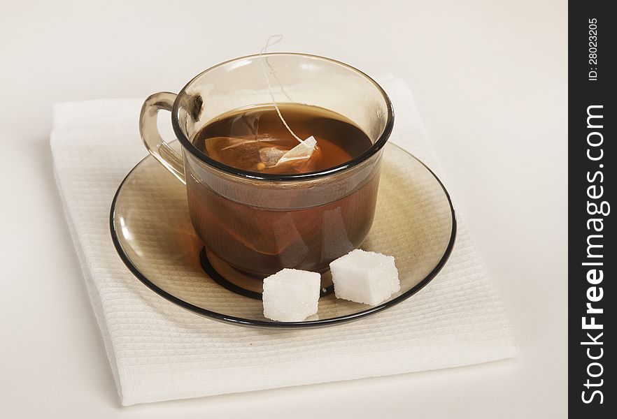 Cup of tea and two slices of sugar on a saucer on a white napkin. Cup of tea and two slices of sugar on a saucer on a white napkin