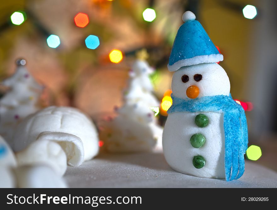 Christmas Cake Decoration snowman, trees and igloo made of sugar. Colourful lights background. Christmas Cake Decoration snowman, trees and igloo made of sugar. Colourful lights background
