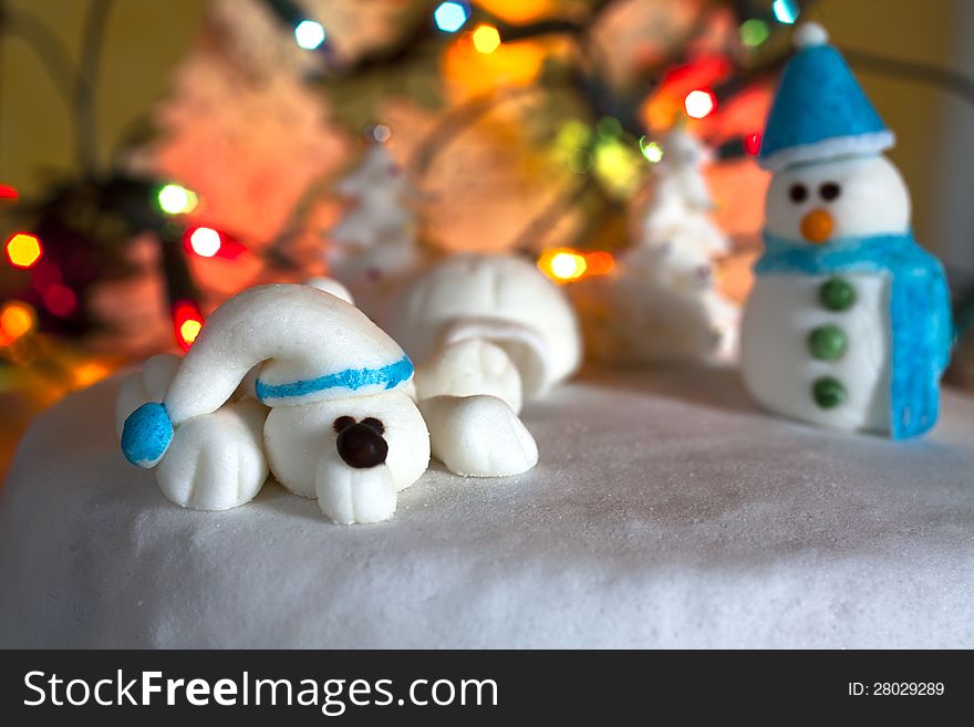 Christmas Cake Decoration snowman, white bear, trees and igloo made of sugar. Colourful lights background