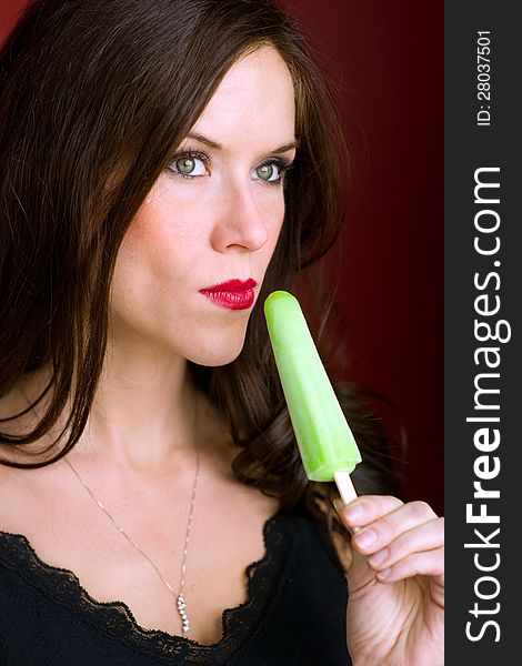 A beautiful brunette has a frozen treat looking off camera. A beautiful brunette has a frozen treat looking off camera