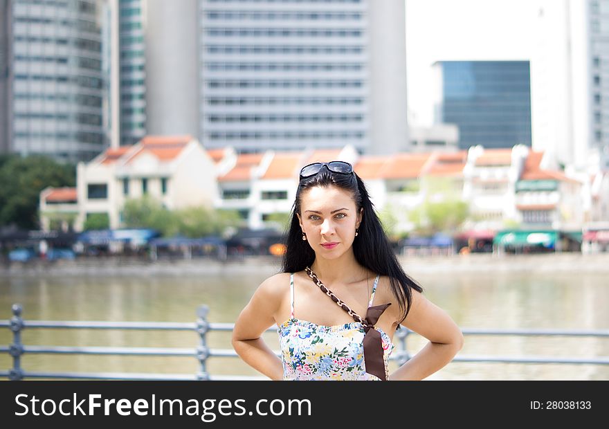 Beautiful brunette posing at riverbank with buildings in background