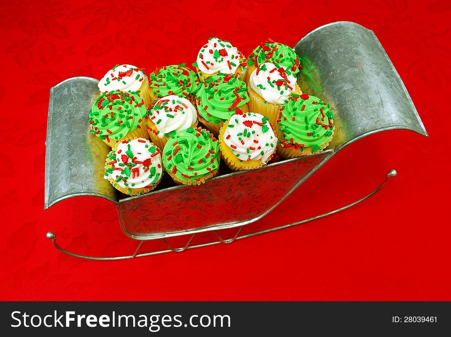 Festive cupcakes displayed in Santa's sleigh. The sleigh sits on a poinsettia-decorated tablecloth. Festive cupcakes displayed in Santa's sleigh. The sleigh sits on a poinsettia-decorated tablecloth.
