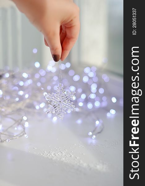 Amid garlands of lights female hand holds a toy snowflake. Amid garlands of lights female hand holds a toy snowflake
