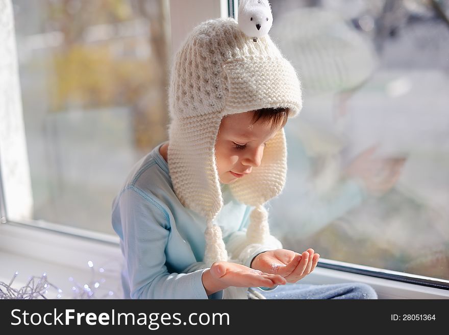 Winter boy sitting by the window in a white knitted cap. Winter boy sitting by the window in a white knitted cap