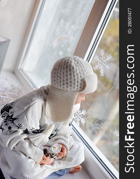 Winter boy sitting by the window in a white knitted cap. Winter boy sitting by the window in a white knitted cap