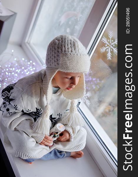 Winter boy sitting by the window in a white knitted cap. Winter boy sitting by the window in a white knitted cap