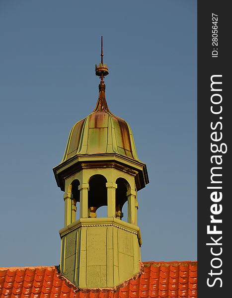A small green copper spire is seen on a red tiled rooftop against the blue sky