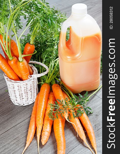 Fresh carrot juice in big plastic bottle alongside with healthy carrots