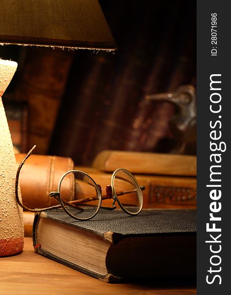 Vintage still life with old spectacles on book near desk lamp