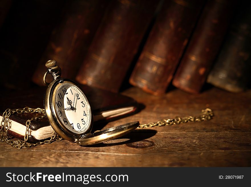 Vintage pocket watch on wooden surface against old books