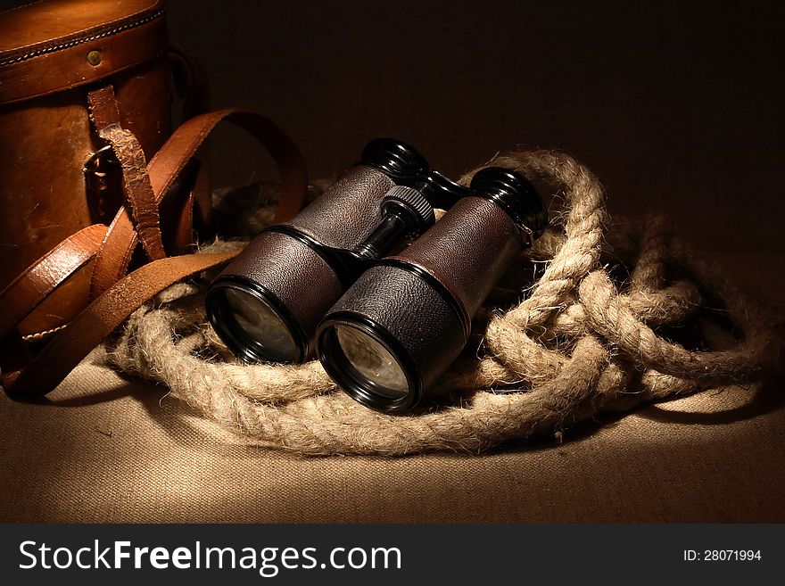 Still life with old binoculars on hemp rope near leather case