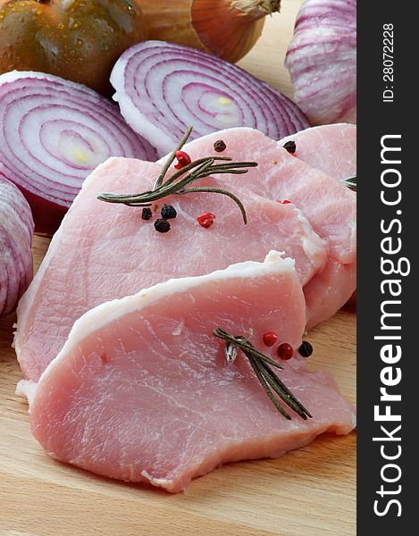 Arrangement of Raw Pork Loin Chops with Rosemary, Peppercorn and Onions on Wood Cutting Board closeup