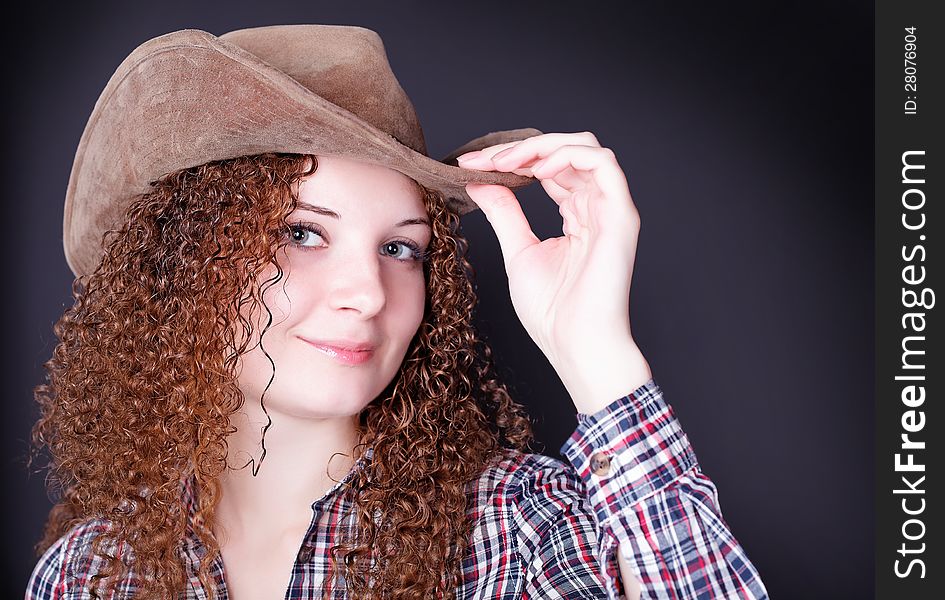 Portrait of a pretty curly girl the cowboy on a dark background