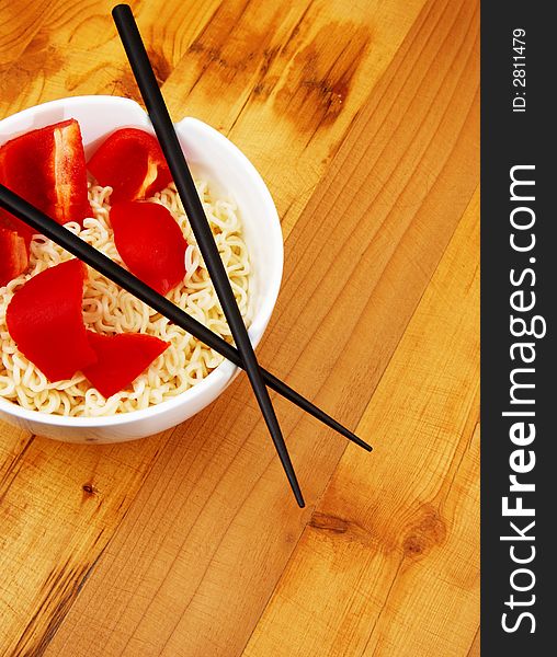 Chinece noodles with chop sticks in a bowl on wooden counter with some peppers in the noodles. Chinece noodles with chop sticks in a bowl on wooden counter with some peppers in the noodles