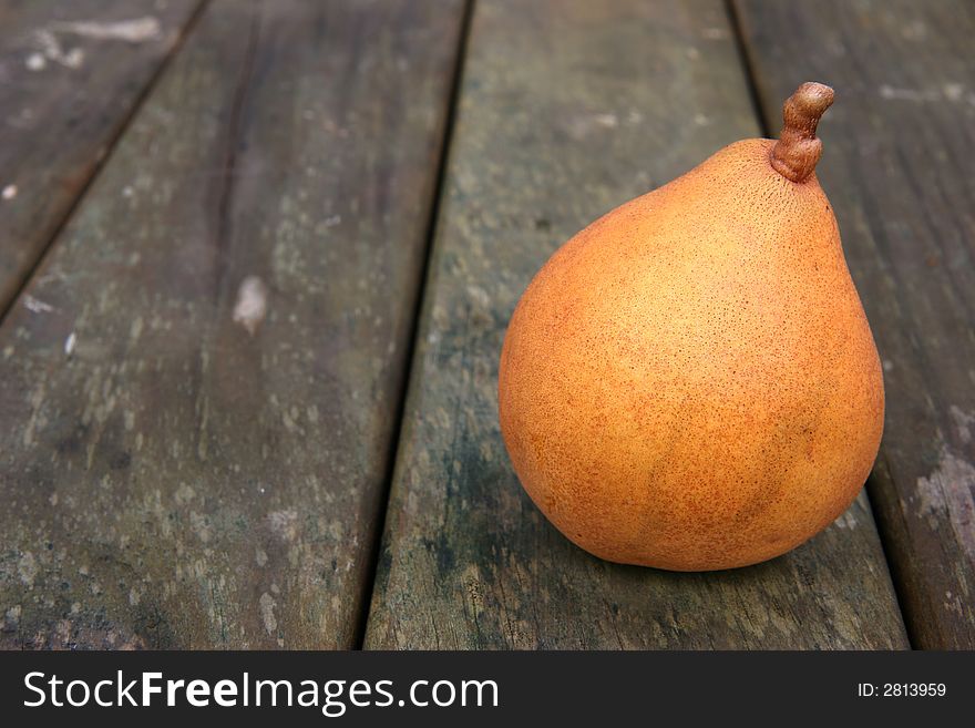 A yellow brown ripe pear on a weathered wooden park table