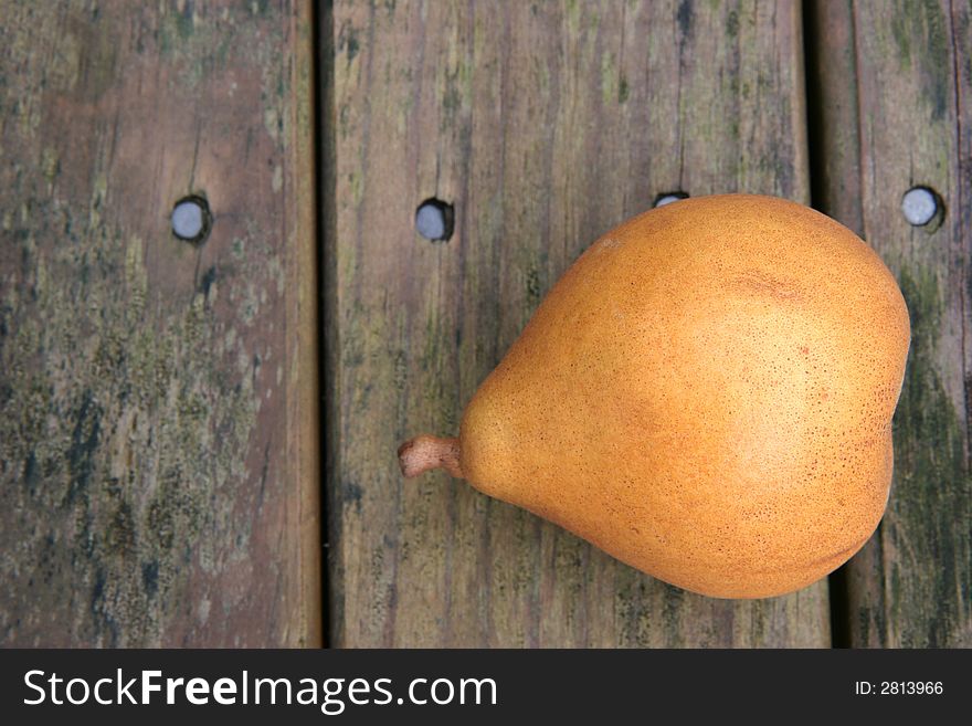 A yellow brown ripe pear on a weathered wooden park table