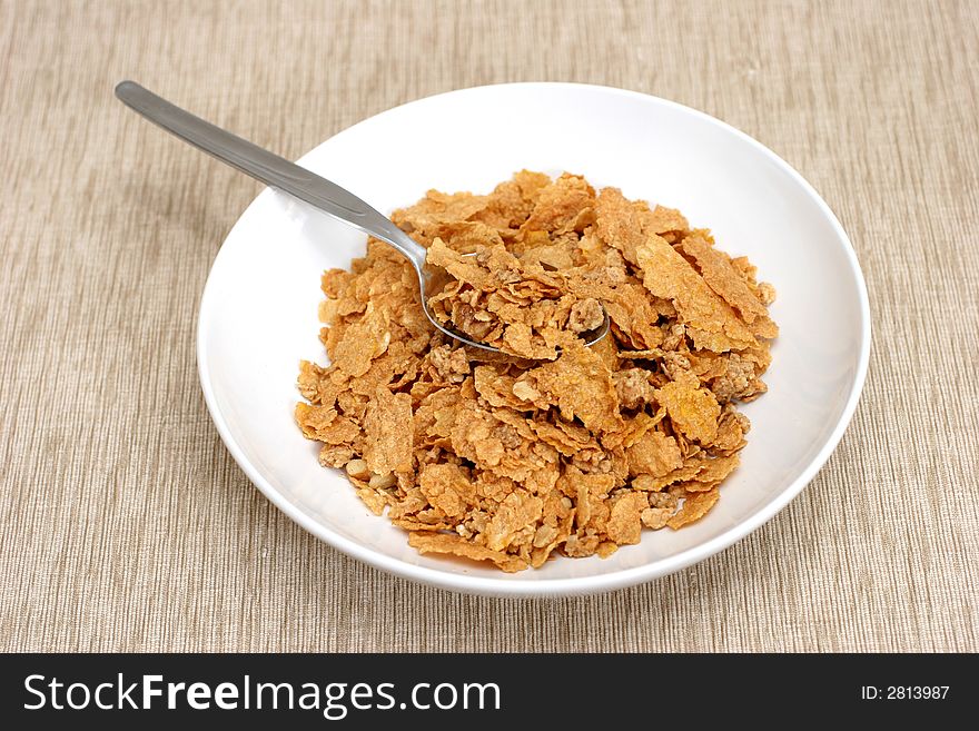 Simple bowl and cornflakes on a brownish beige mat. Simple bowl and cornflakes on a brownish beige mat