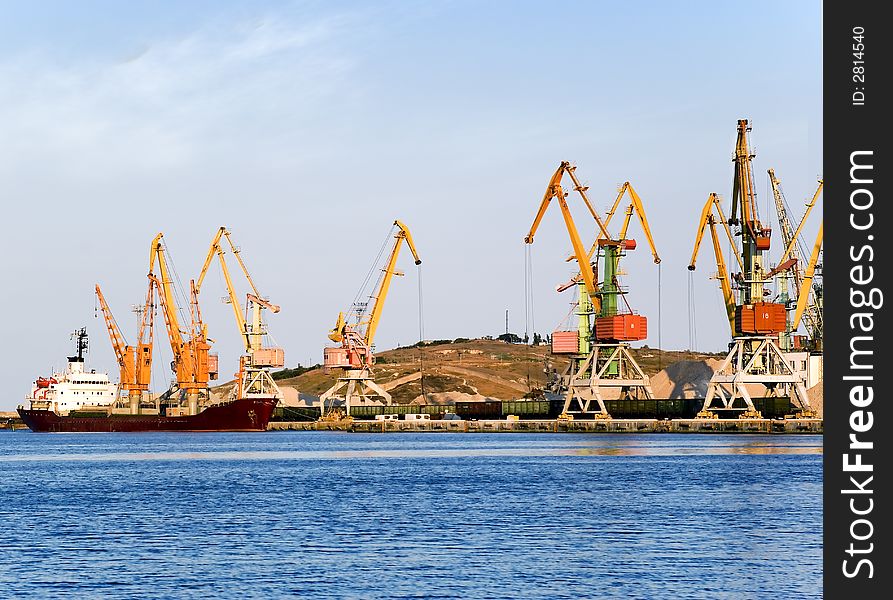 Seaport on a background of picturesque mountains. Elevating cranes with bright colors