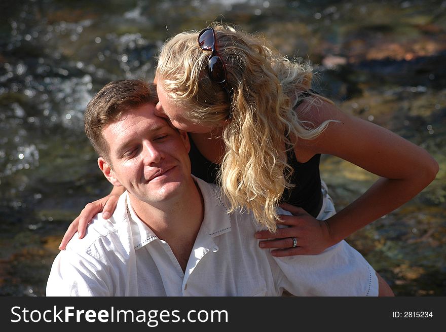 A happy couple sits on a rock in a river. A happy couple sits on a rock in a river.