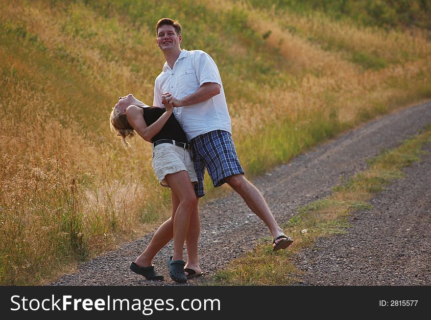 A young couple jokes around while walking down a dirt road in the countryside. A young couple jokes around while walking down a dirt road in the countryside.