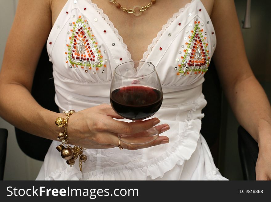 The woman in a white dress holds a wine glass with red wine. The woman in a white dress holds a wine glass with red wine