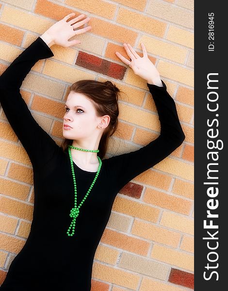 Serious teen in black pressed against a bright wall with her hands overhead. Serious teen in black pressed against a bright wall with her hands overhead.