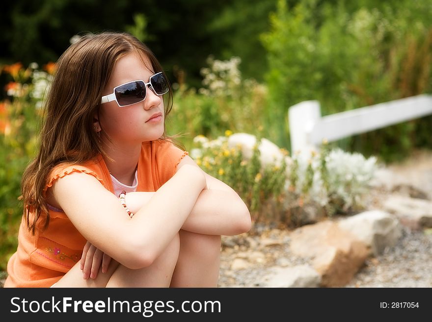 Portrait of an attractive preteen in a sunny garden gazing into the distance through her sunglasses. Portrait of an attractive preteen in a sunny garden gazing into the distance through her sunglasses.