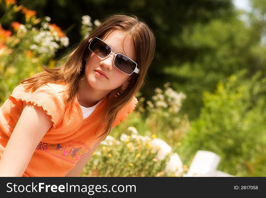 Portrait of an attractive preteen in a sunny garden gazing toward the viewer through her sunglasses. Portrait of an attractive preteen in a sunny garden gazing toward the viewer through her sunglasses.