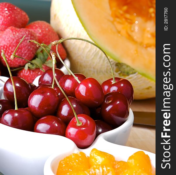 Small bowls of strawberries, cherries, and mandarin orange slices with a cantaloupe in the back. Small bowls of strawberries, cherries, and mandarin orange slices with a cantaloupe in the back.